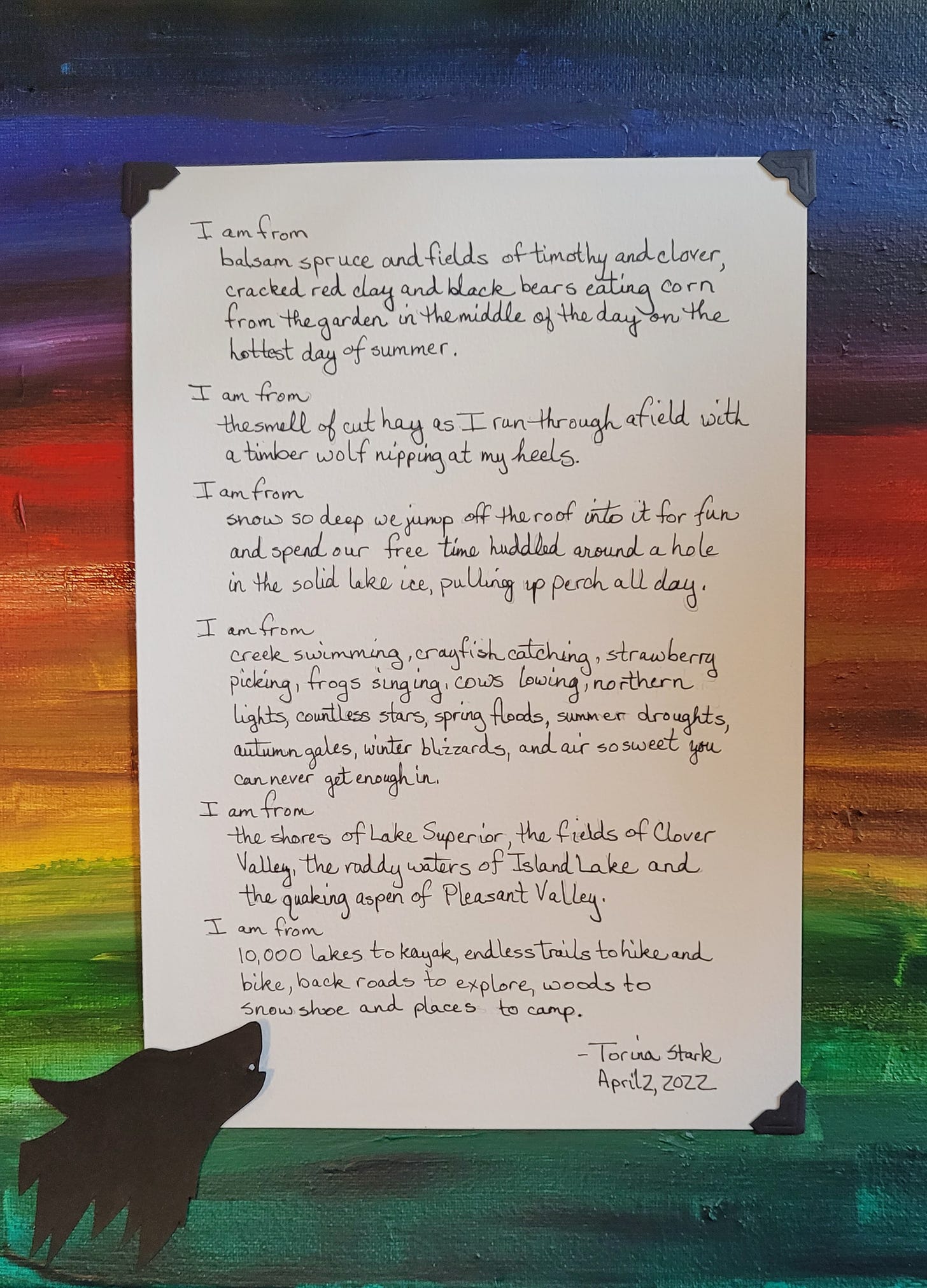 "I Am From" poem mounted on rainbow painted canvas with a howling wolf out of black cut paper