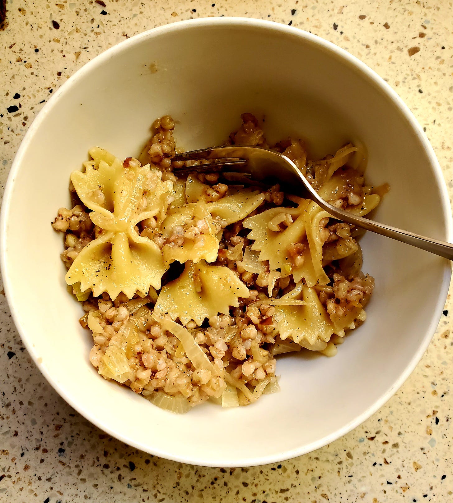 A white bowl with bow tie pasta, kasha groats, and browned onions in it. 