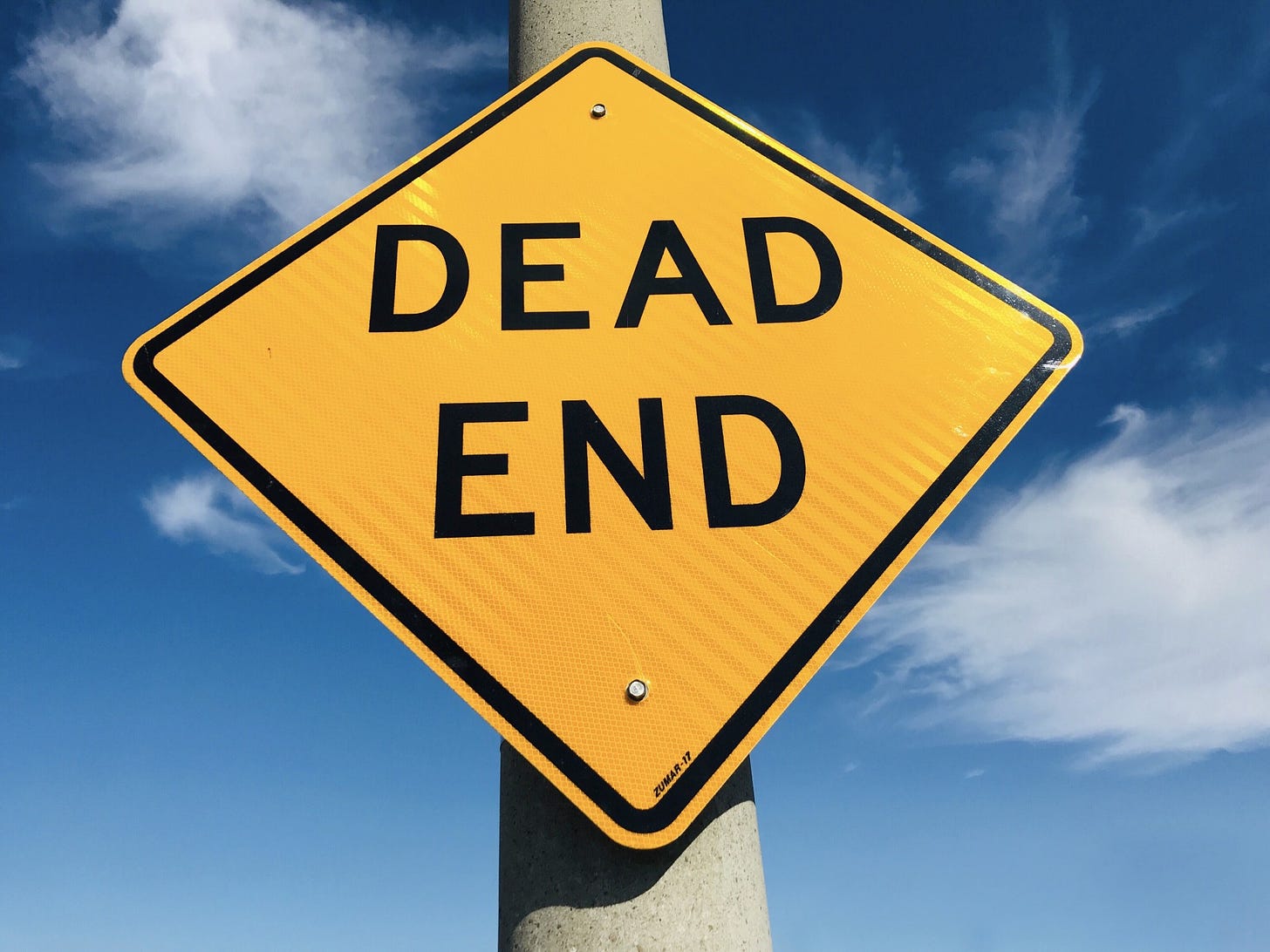 A bright yellow sign stands against a blue sky and reads, “Dead end.”