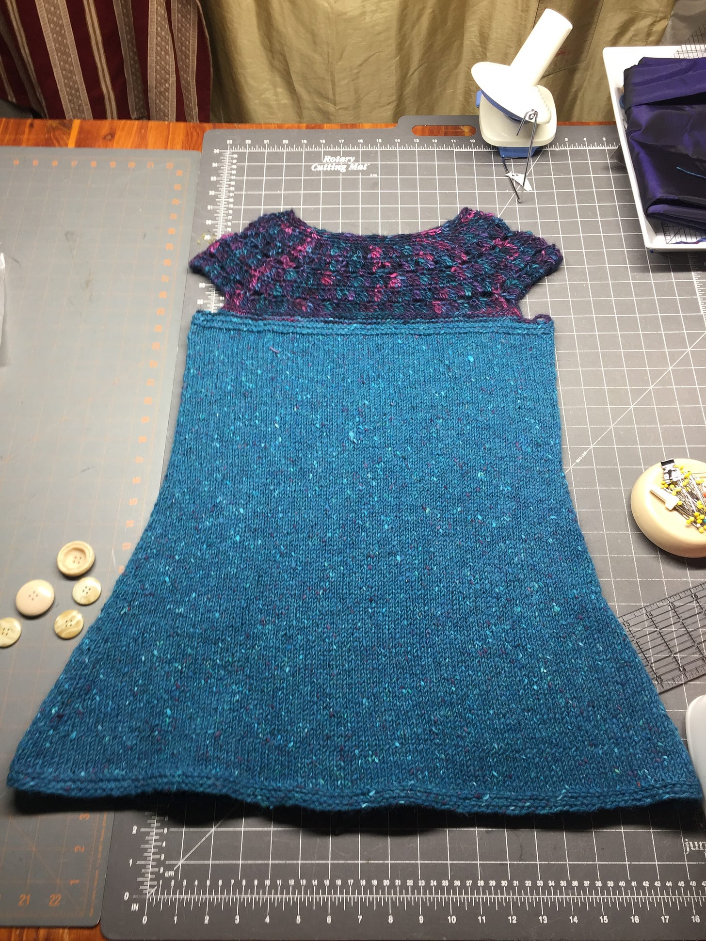A handknitted teal sweater with a dark colored yoke. 