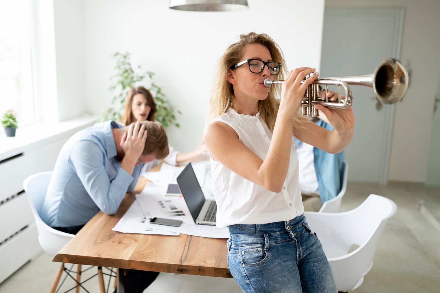 A friend plays a loud horn obnoxiously while her other friends have a business meeting.