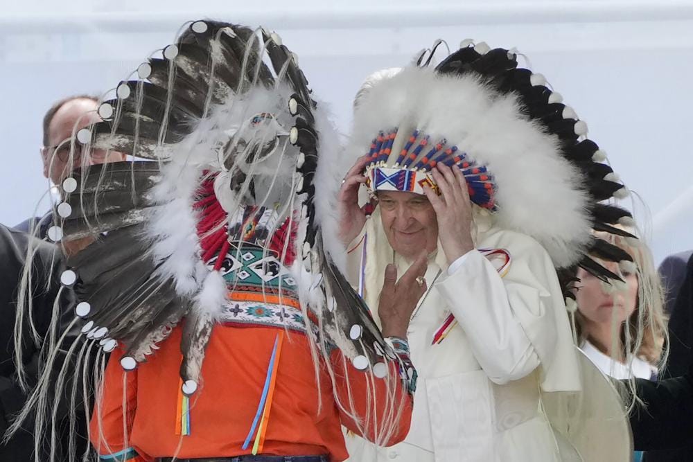Pope Francis puts on an indigenous headdress during a meeting with indigenous communities, including First Nations, Metis and Inuit, at Our Lady of Seven Sorrows Catholic Church in Maskwacis, near Edmonton, Canada, Monday, July 25, 2022. Pope Francis begins a "penitential" visit to Canada to beg forgiveness from survivors of the country's residential schools, where Catholic missionaries contributed to the "cultural genocide" of generations of Indigenous children by trying to stamp out their languages, cultures and traditions. Francis set to visit the cemetery at the former residential school in Maskwacis. (AP Photo/Gregorio Borgia)