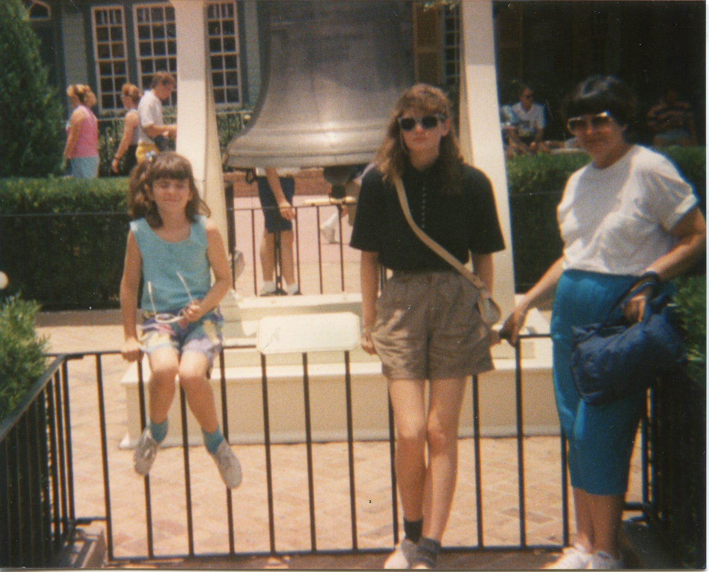 Three white people, a young girl, a teenager, and a mother, next to a fake Liberty Bell. 