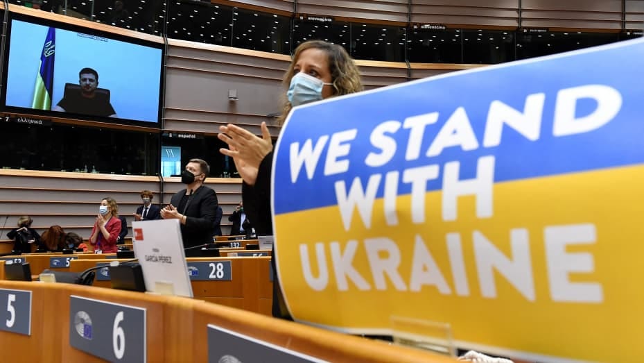 Members of the European Parliament applaud Ukrainian President Volodymyr Zelensky who appears on a screen as he speaks in a video conference during a special plenary session of the European Parliament focused on the Russian invasion of Ukraine at the EU h