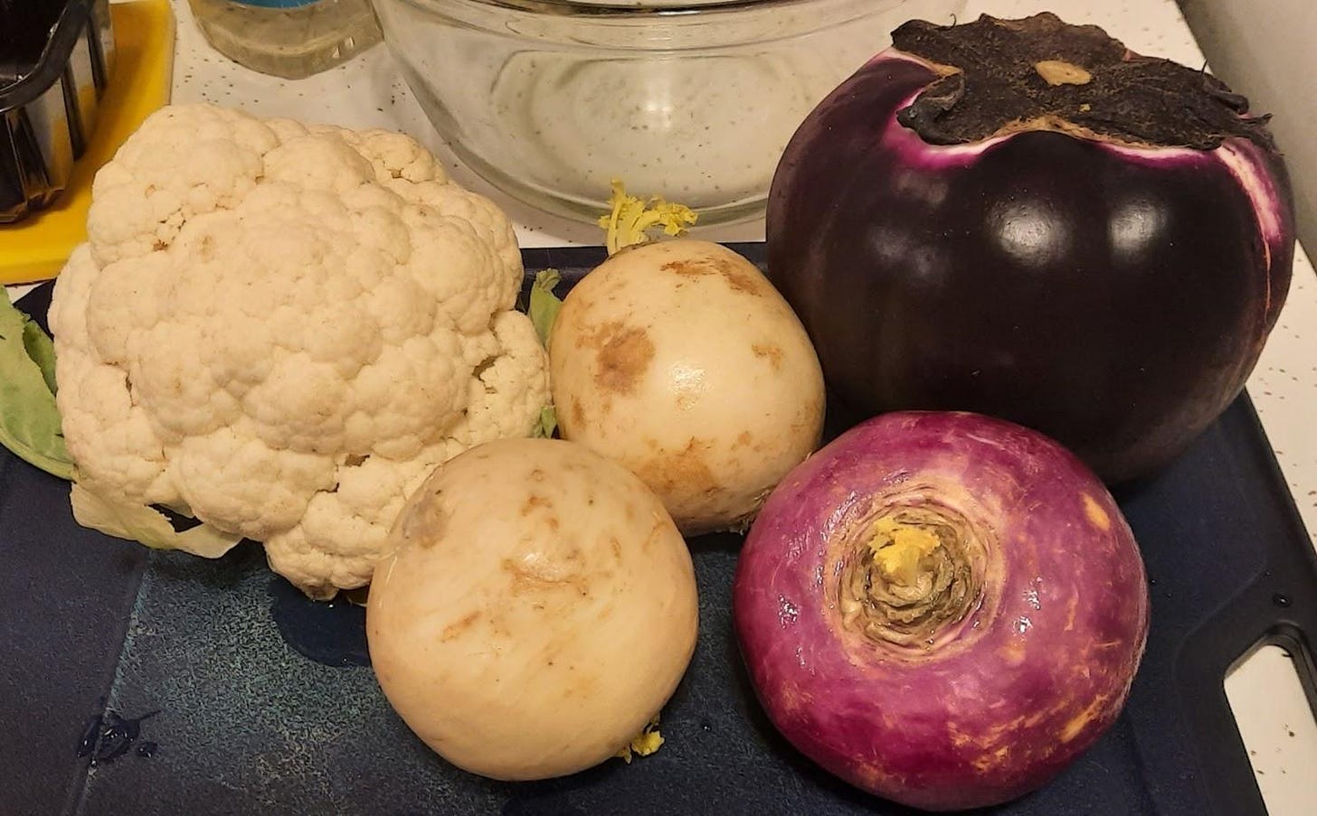 Cauliflower, turnips and eggplant on a blue chopping board.