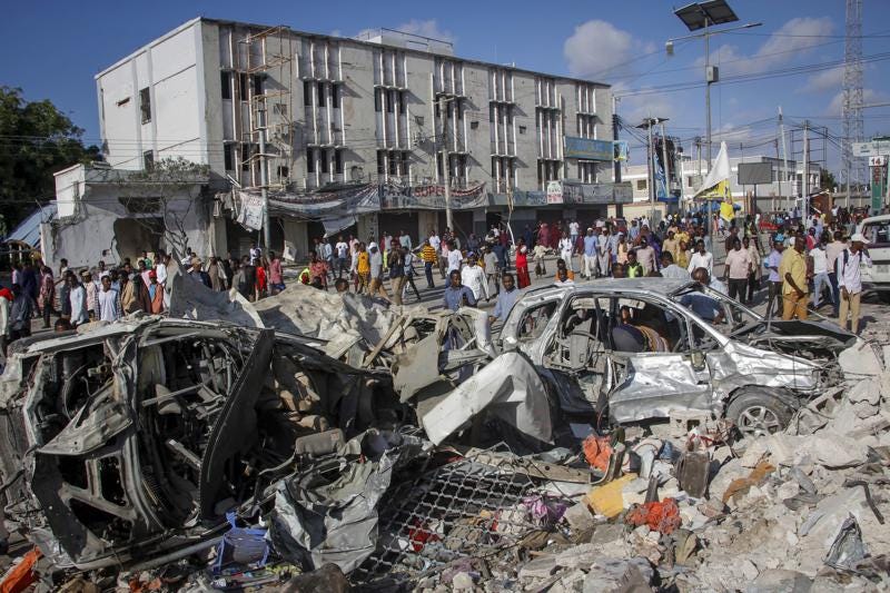 People walk amidst destruction at the scene, a day after a double car bomb attack at a busy junction in Mogadishu, Somalia Sunday, Oct. 30, 2022. Somalia's president says multiple people were killed in Saturday's attacks and the toll could rise in the country's deadliest attack since a truck bombing at the same spot five years ago killed more than 500. (AP Photo/Farah Abdi Warsameh)