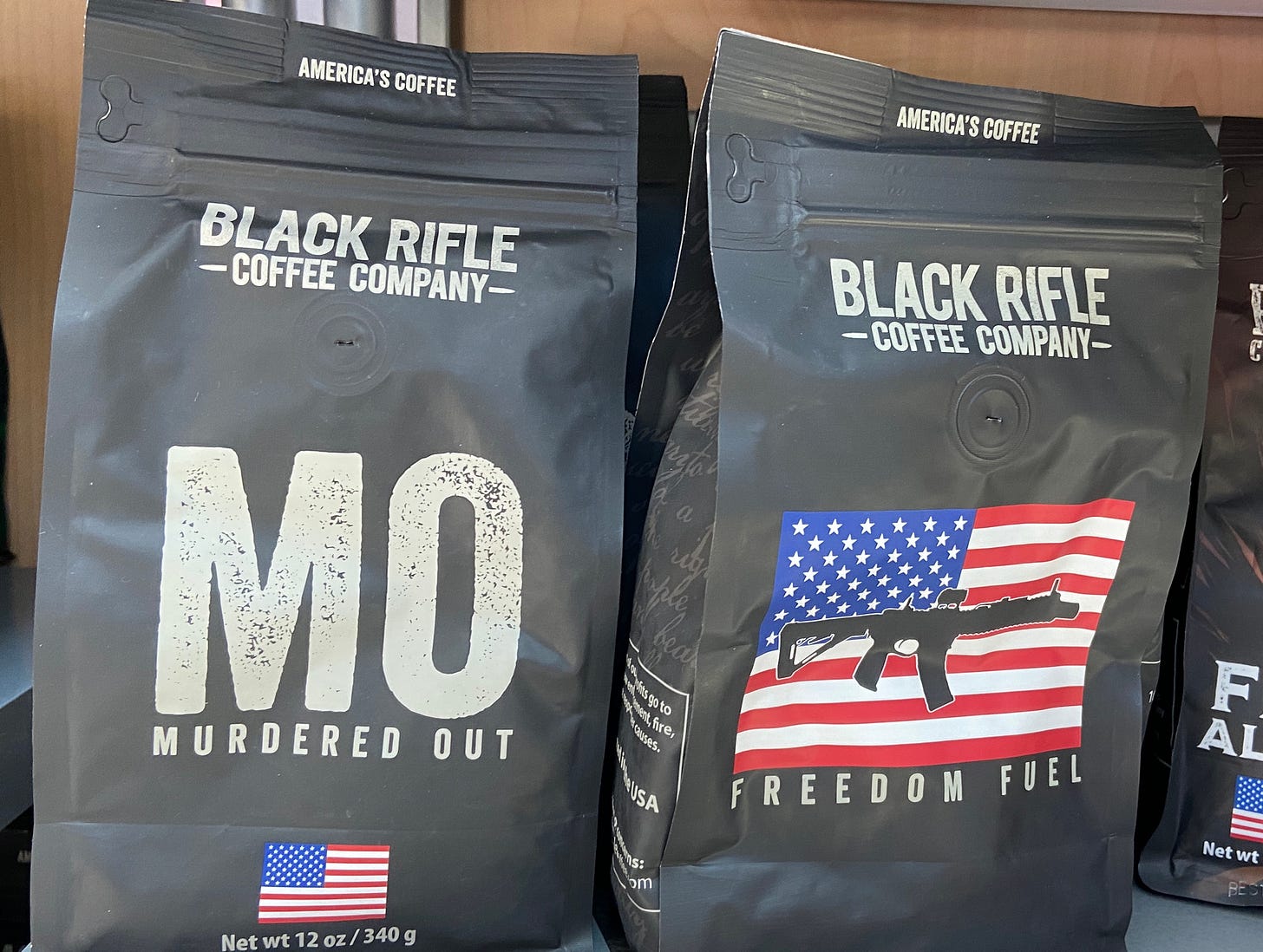 An image of two bags of coffee, one named "Murdered Out" and the other "Freedom Fuel." Images of the american flag and assault weapons are shown on the bag design.