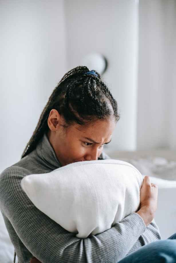 crying black woman hugging pillow in bedroom