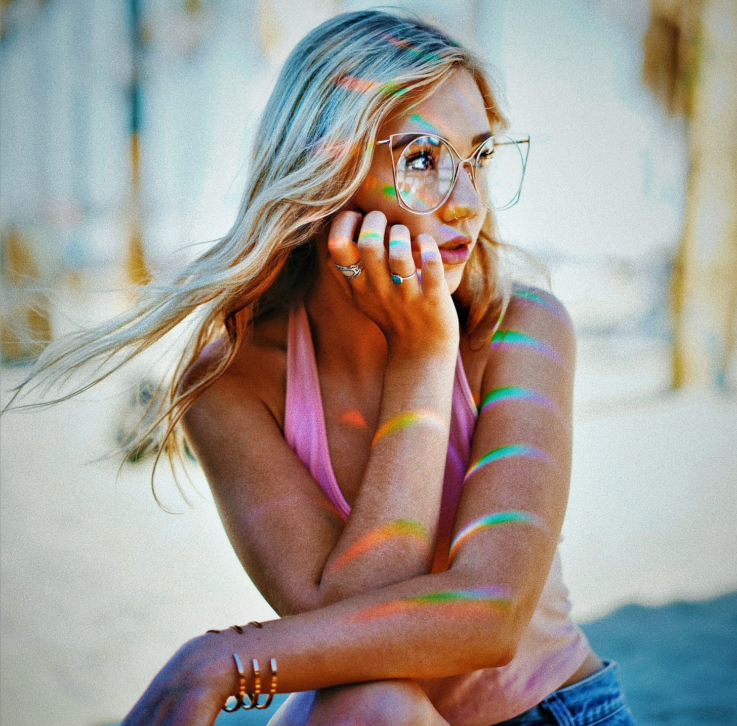 girl with blonde hair and glasses with hand on cheek colorful highlights on her arms