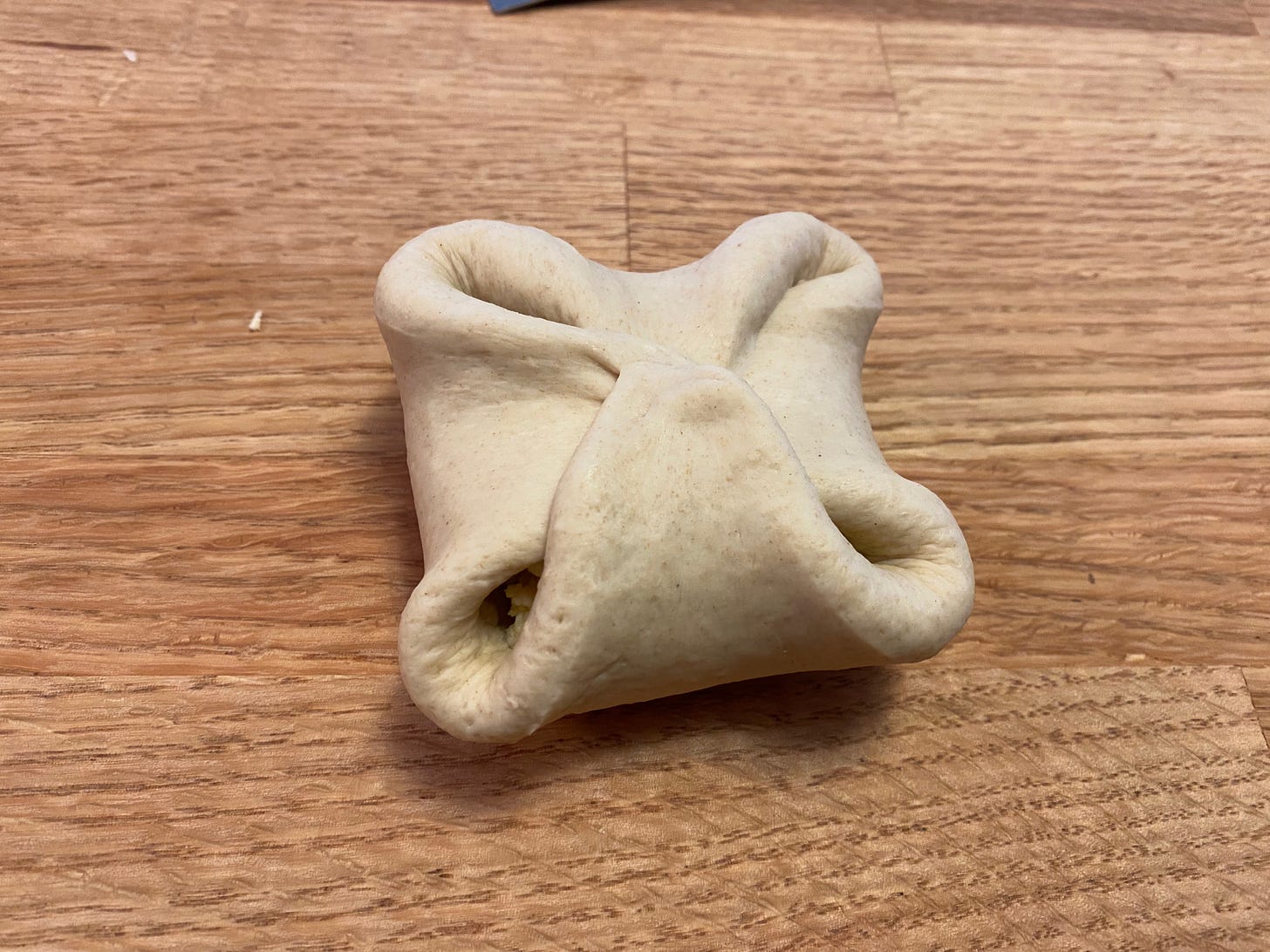 The four sides of the dough have now been folded up and in, to make a shape like a four leaf clover. There are still gaps at the four corners where the dough doesn’t quite meet.