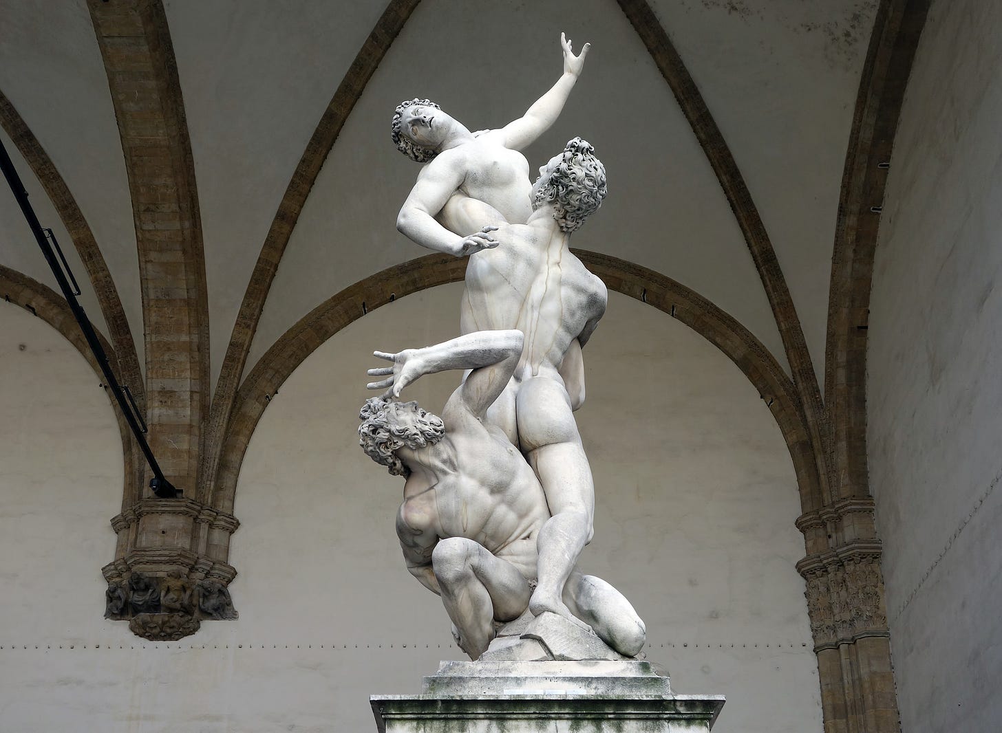 A marble statue of three figures. One man is crouching, while other holds a woman. The woman is reaching out, as if in distress. They are all nude.