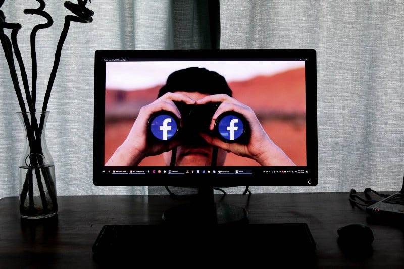 A computer screen with a wallpaper picturing a man looking through binoculars with the Facebook logo on both lenses