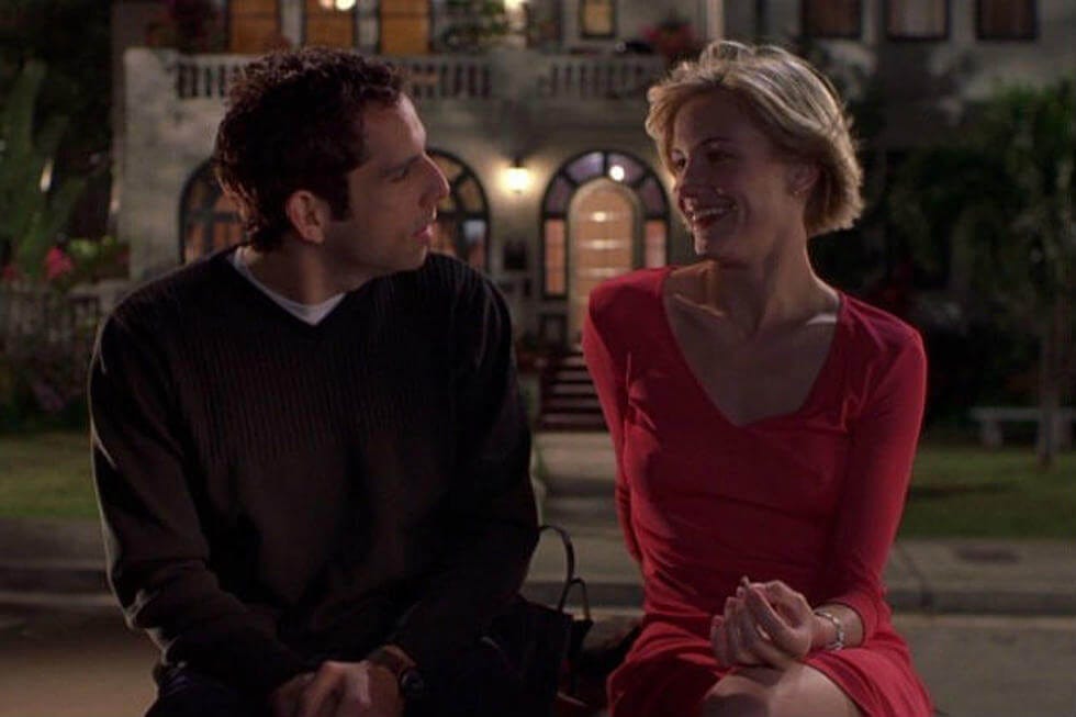 Film still from There's Something About Mary. Ben Stiller and Cameron Diaz sit on a bench at night outside a house, laughing.