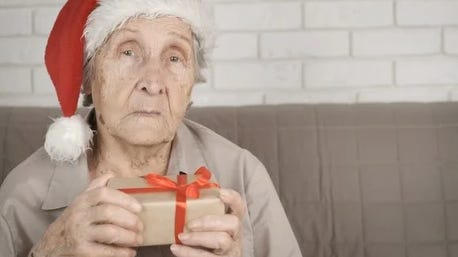 Uma idosa triste com chapéu de Papai Noel segurando um presente