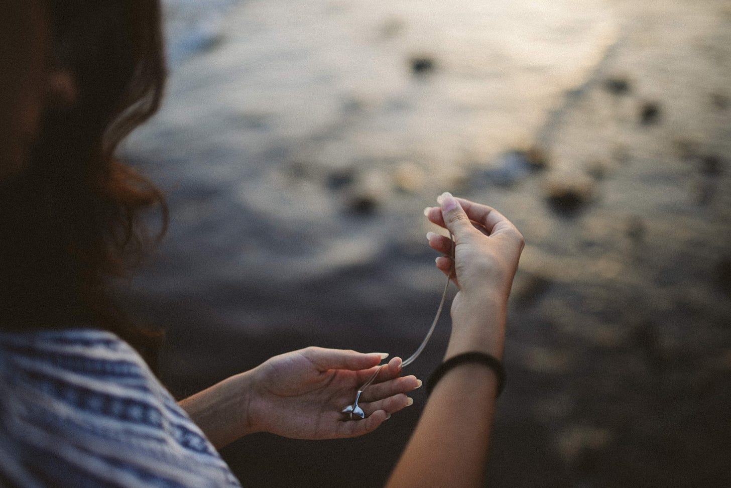 A woman stares longingly at a pendant that she holds in her hand on a beach.