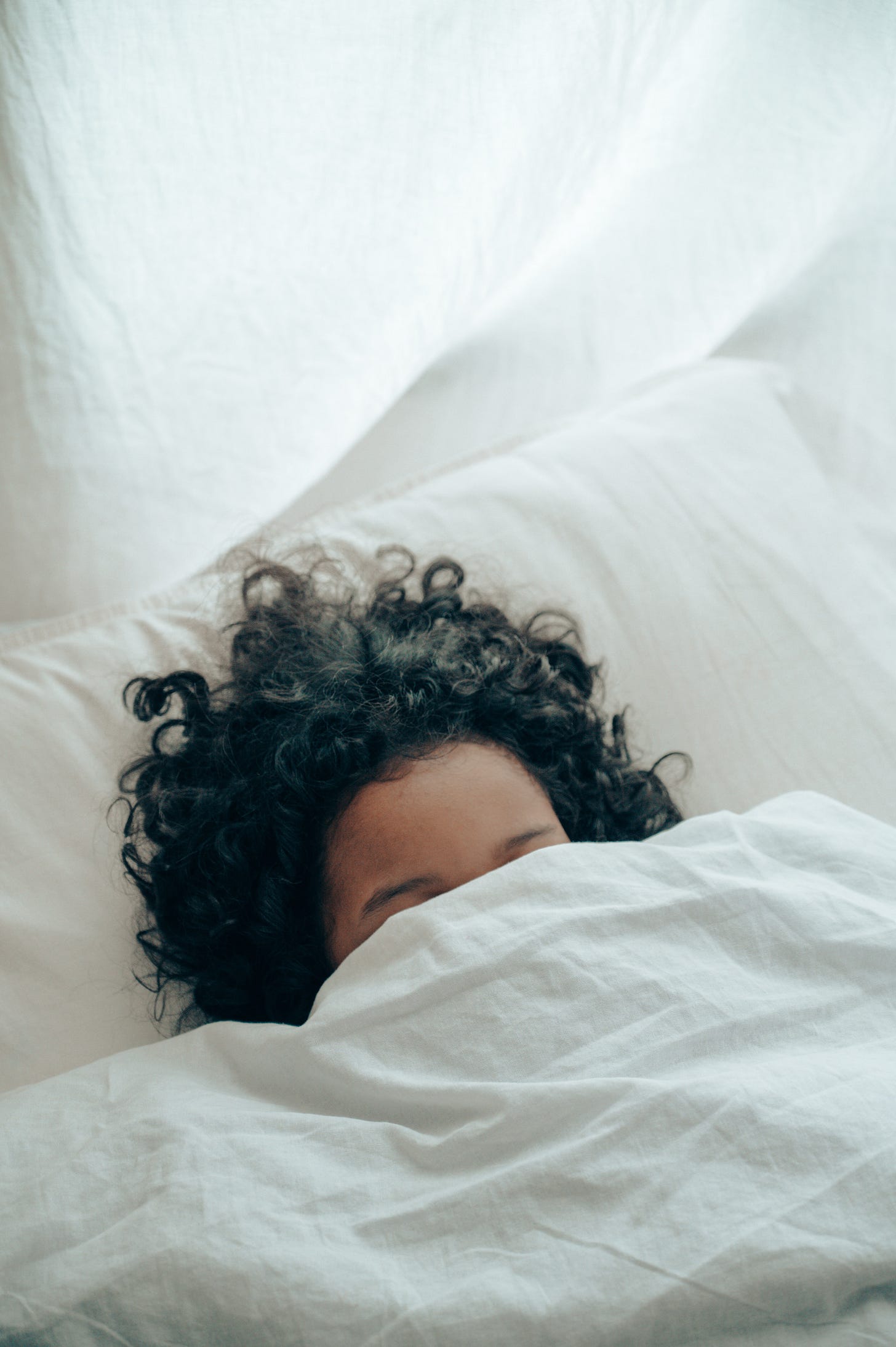 a woman with half of her head out of the covers in bed