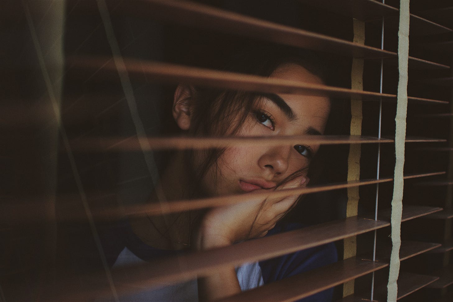 Sad looking thai woman staring through some window blinds
