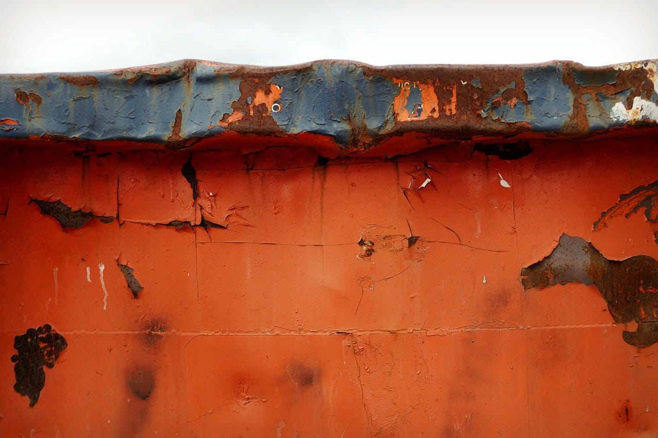 A close up of the rusty red painted edge of a trash dumpster.