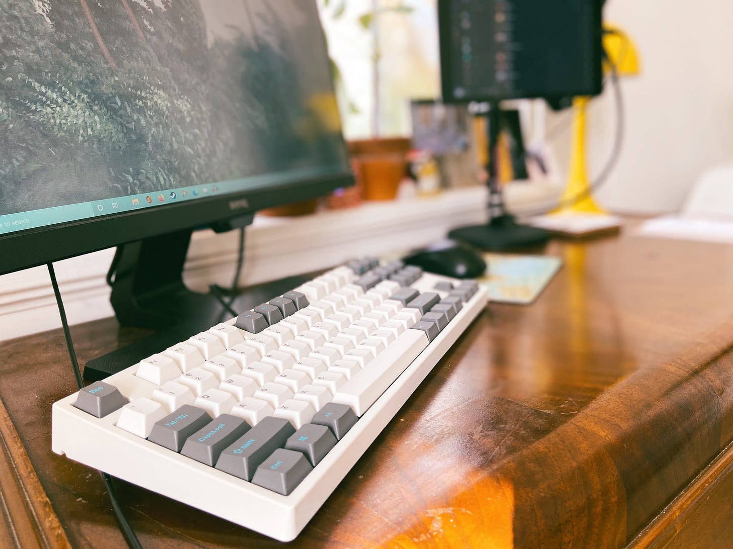 A desktop with computer monitor and mechanical keyboard, with a mouse and elevated tablet visible out of focus in the background