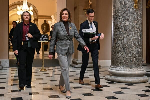 Speaker Nancy Pelosi, wearing a gray suit, walks to her office in the Capitol with two staff members.
