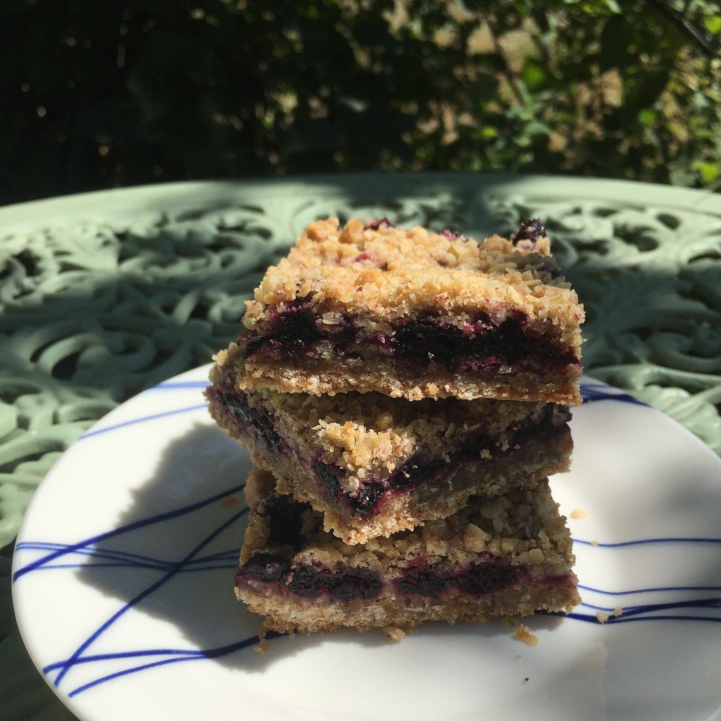 a stack of three offset oat and black raspberry squares on a white plate with blue stripes. 