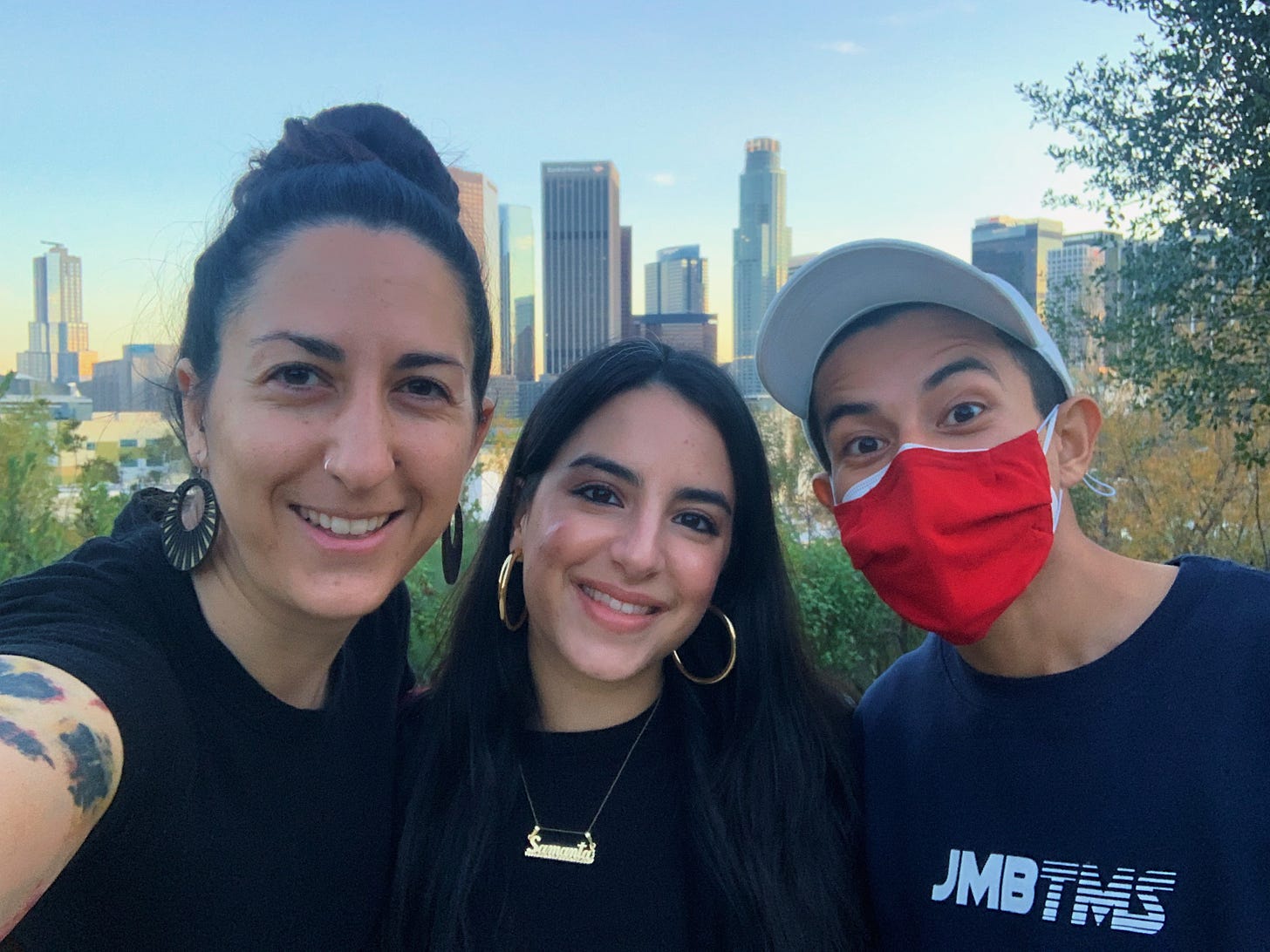 Selfie of Ali, Samanta, and J.T. smiling at the camera with the downtown LA skyline in the background at dusk.