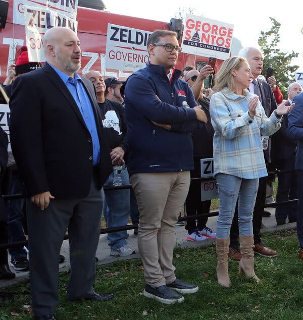 George Santos stands in front of a crowd of people holding political signs with his name and that of the Republican gubernatorial candidate, Lee Zeldin.