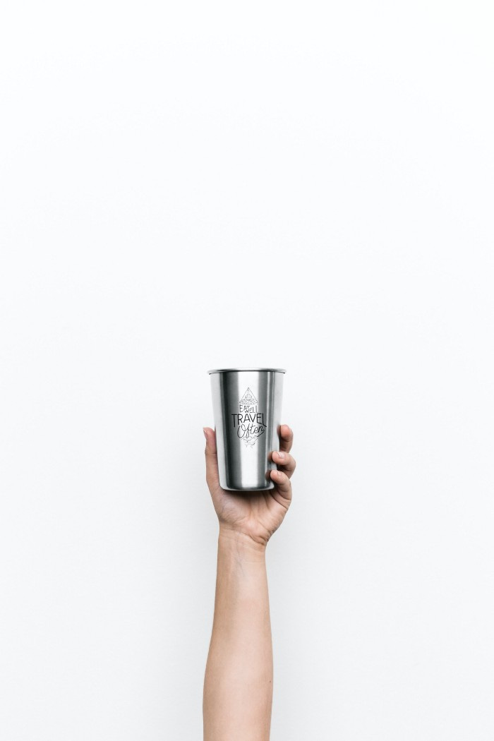 A hand holding a silver mug in the center of the screen. There is nothing but white space around it.