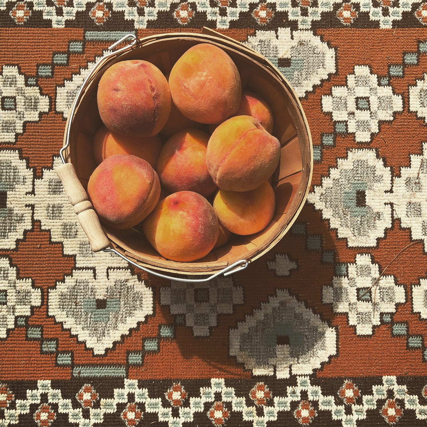 overhead view of basket of peaches on a patterned rug.