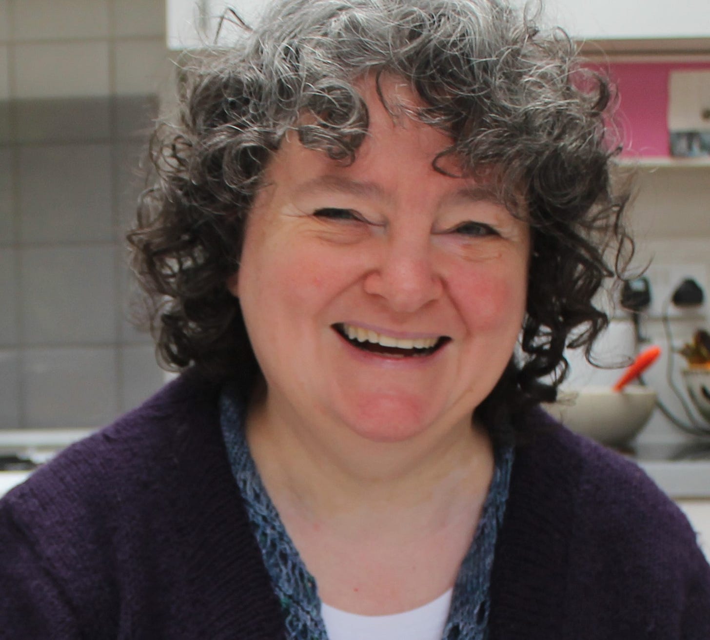 A white women with curly hair wearing a purple handknit sweater.