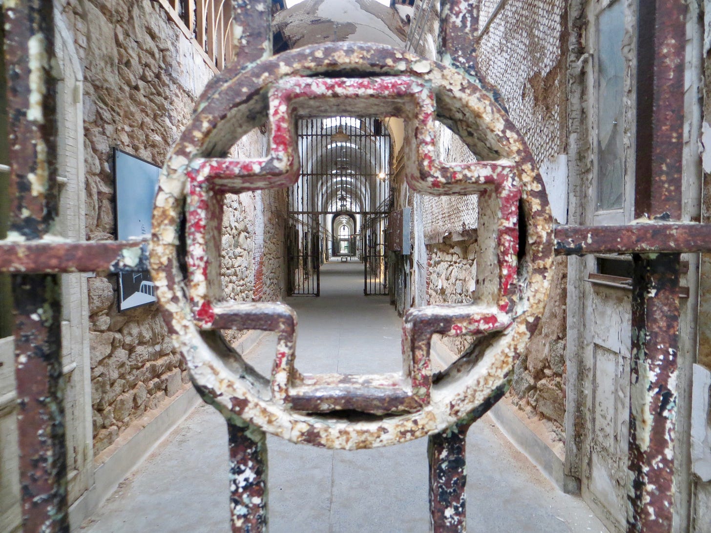 View of a 19th centuray penitentiary hospital wing taken through a corroded metal gate shaped like a cross.