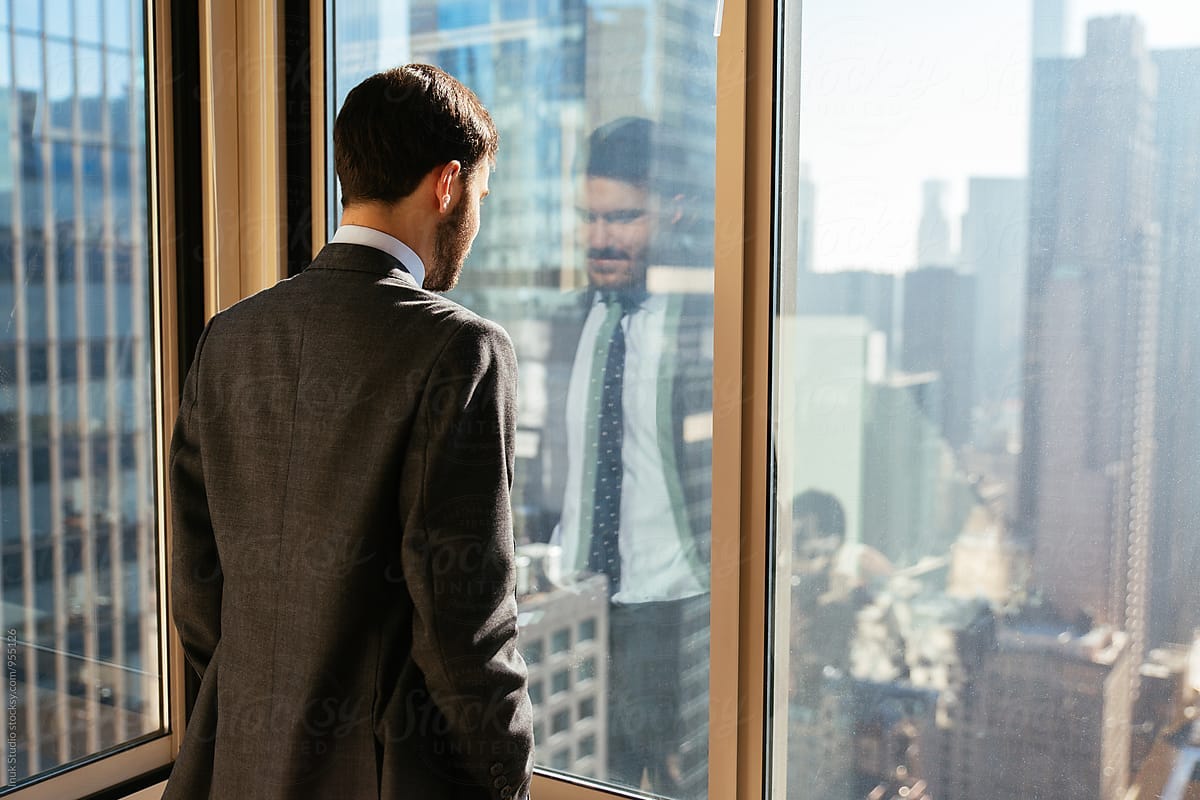 Businessman looking through window at city from the office by Inuk Studio -  Stocksy United