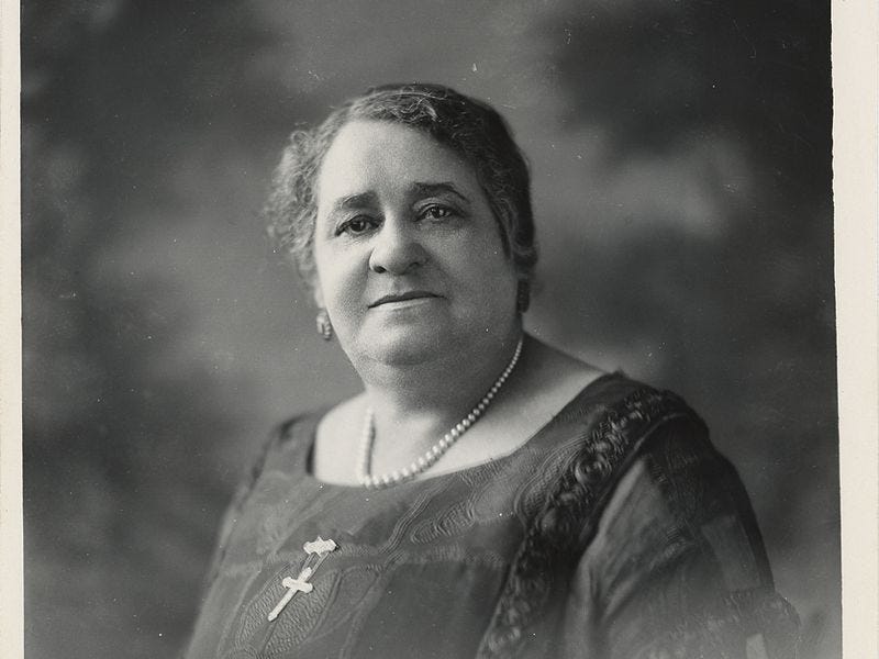 A black and white photo of Maggie Lena Walker, a Black woman, wearing a black dress and a crucifix necklace