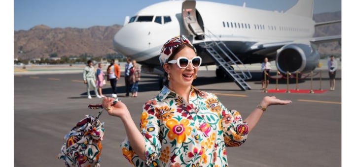 A woman in bright florals smiling in front of a private jet