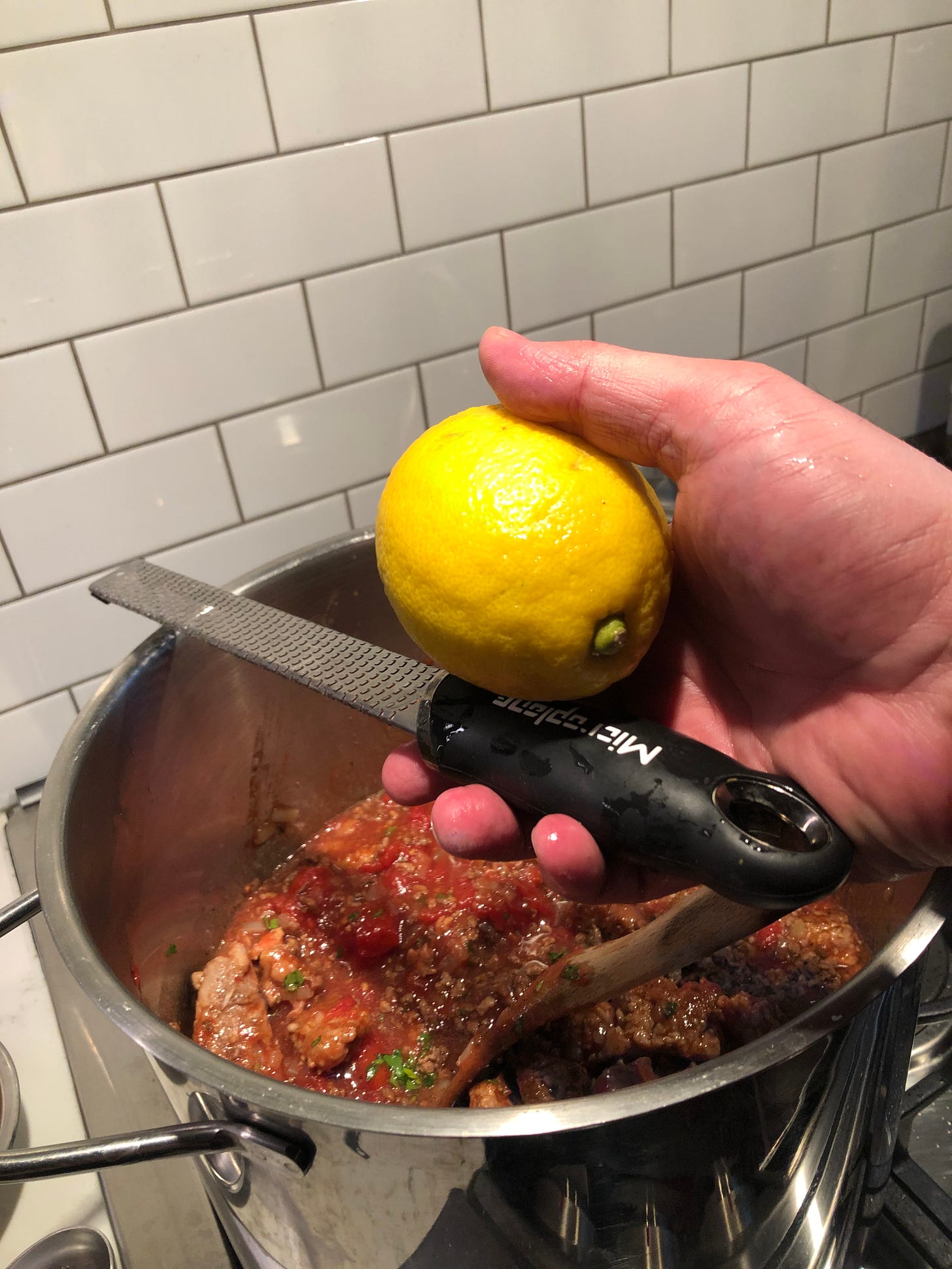 A hand holding a lemon and a Microplane grater over the pot of sauce