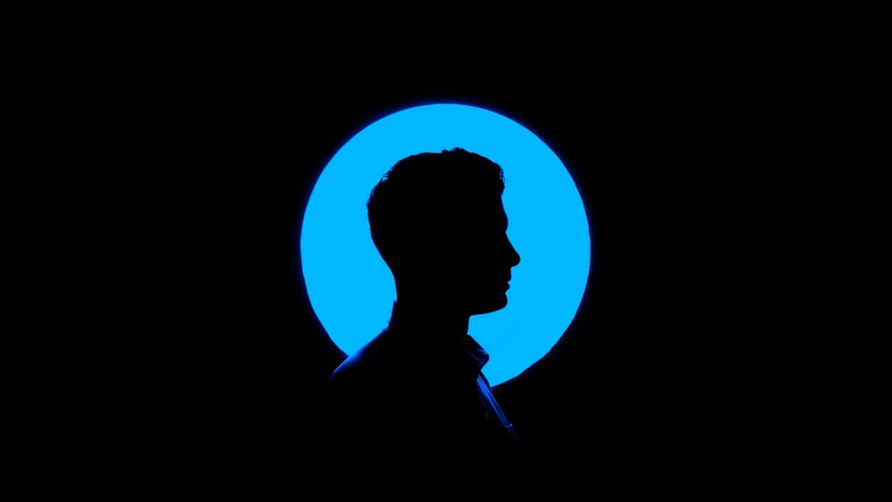 Right-facing silhouette of a man in front of a blue disc on a black background