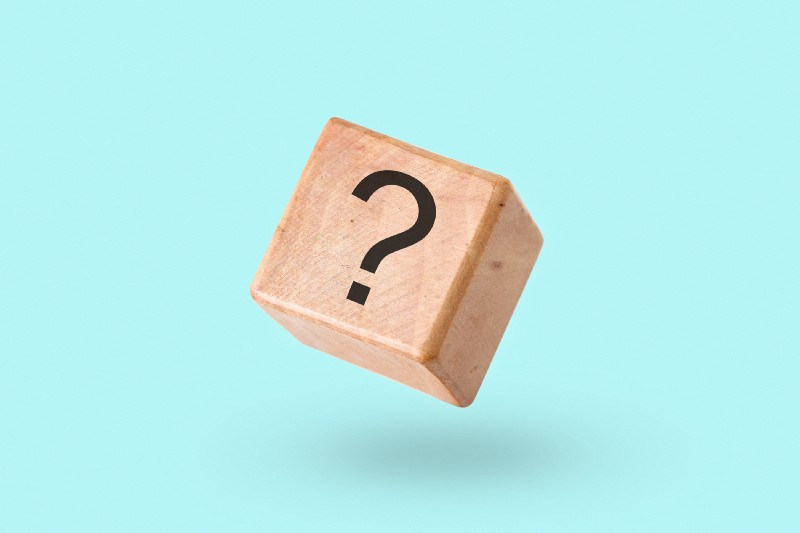 A wooden cube with a question mark on its front stands against a blue background.