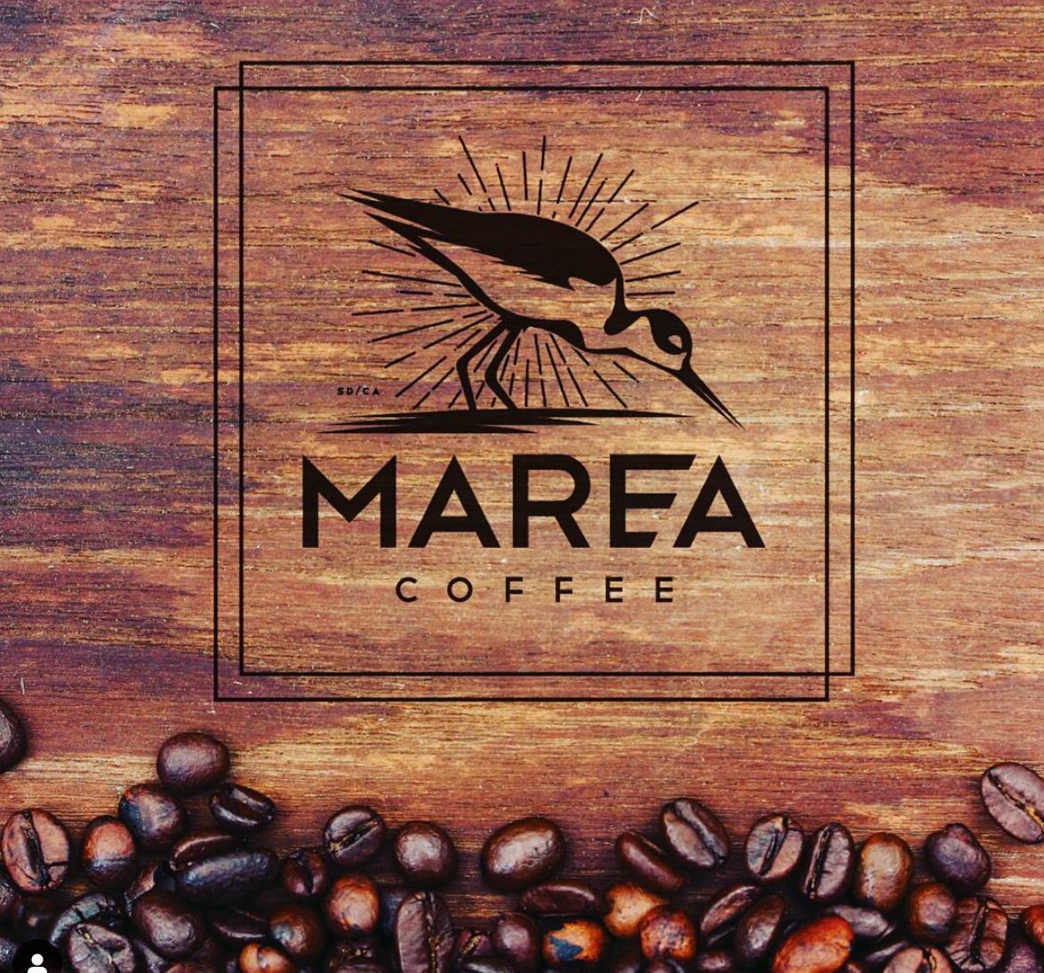 Marea Coffee logo of a bird superimposed over a piece of stained brown wood with coffee beans sprinkled along the bottom.