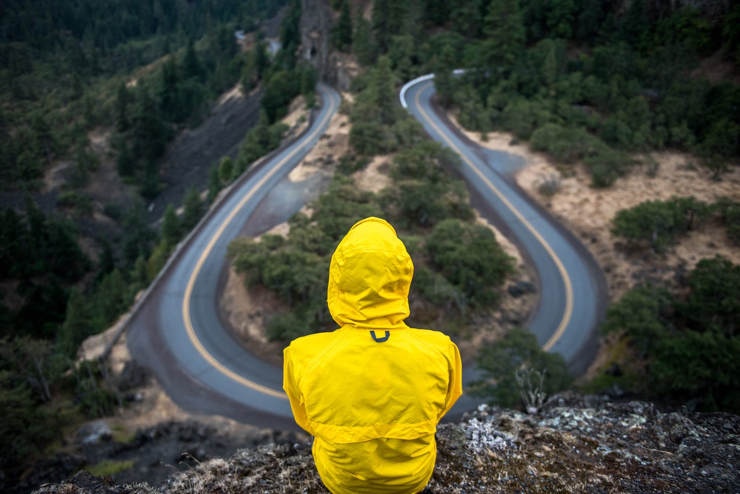 Person in yellow rain jacket looking at two roads that going in opposite directions.