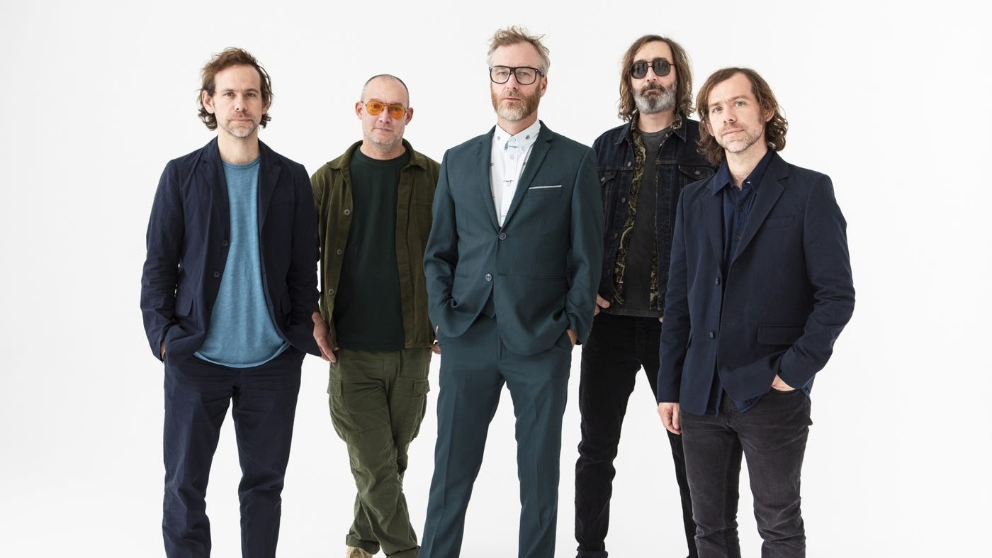 The National, a group of middle-aged white men wearing variously suits and jackets and t-shirts. They are standing against a white background and visibly attempting to look cool