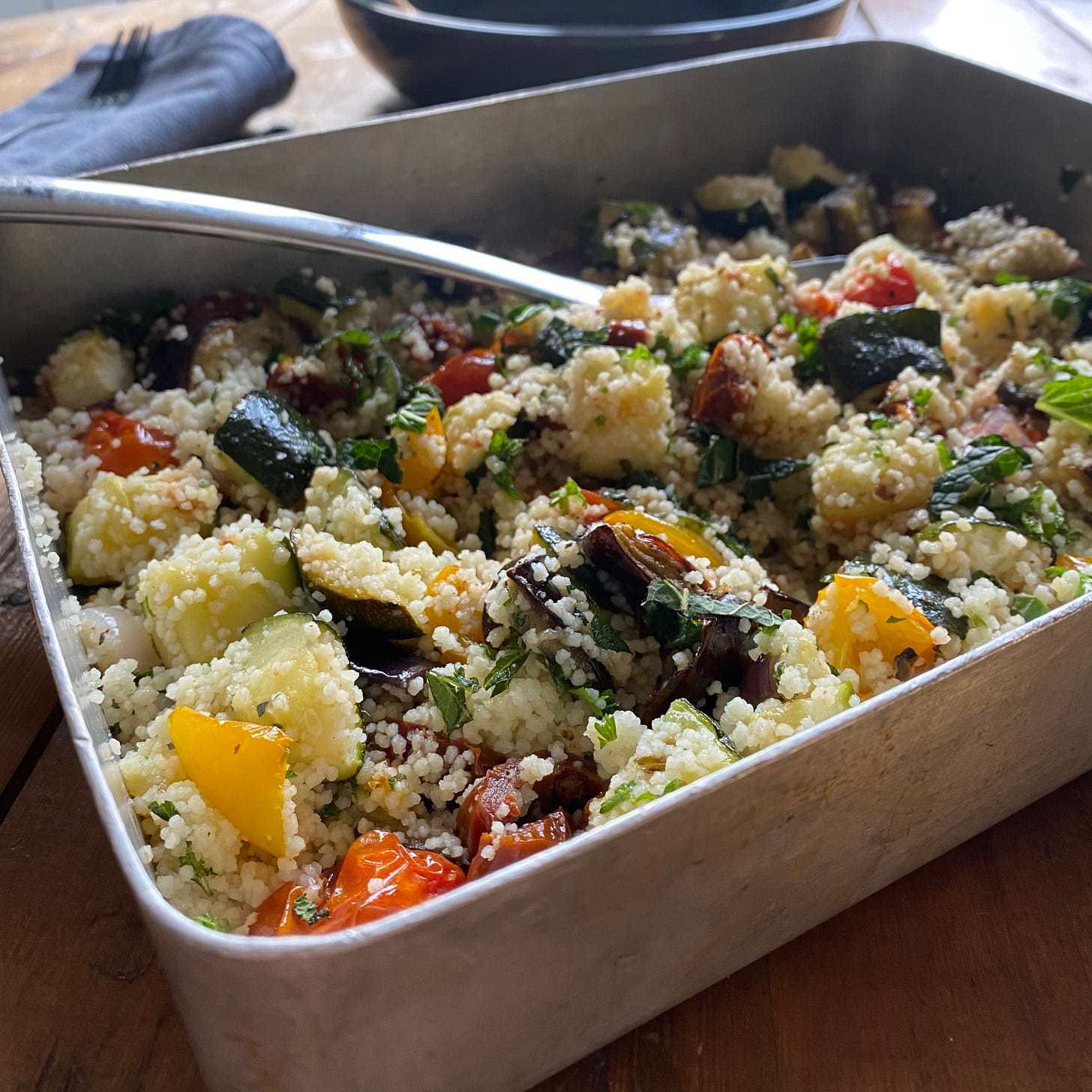 Aluminium oven tray filled with roasted courgette, aubergine, peppers, onion and tomatoes stirred through cous cous