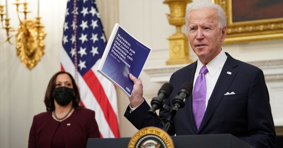 President Joe Biden signs an executive order as Vice President Kamala Harris looks on during an event on economic crisis in the State Dining Room of the White House Friday in Washington, D.C.