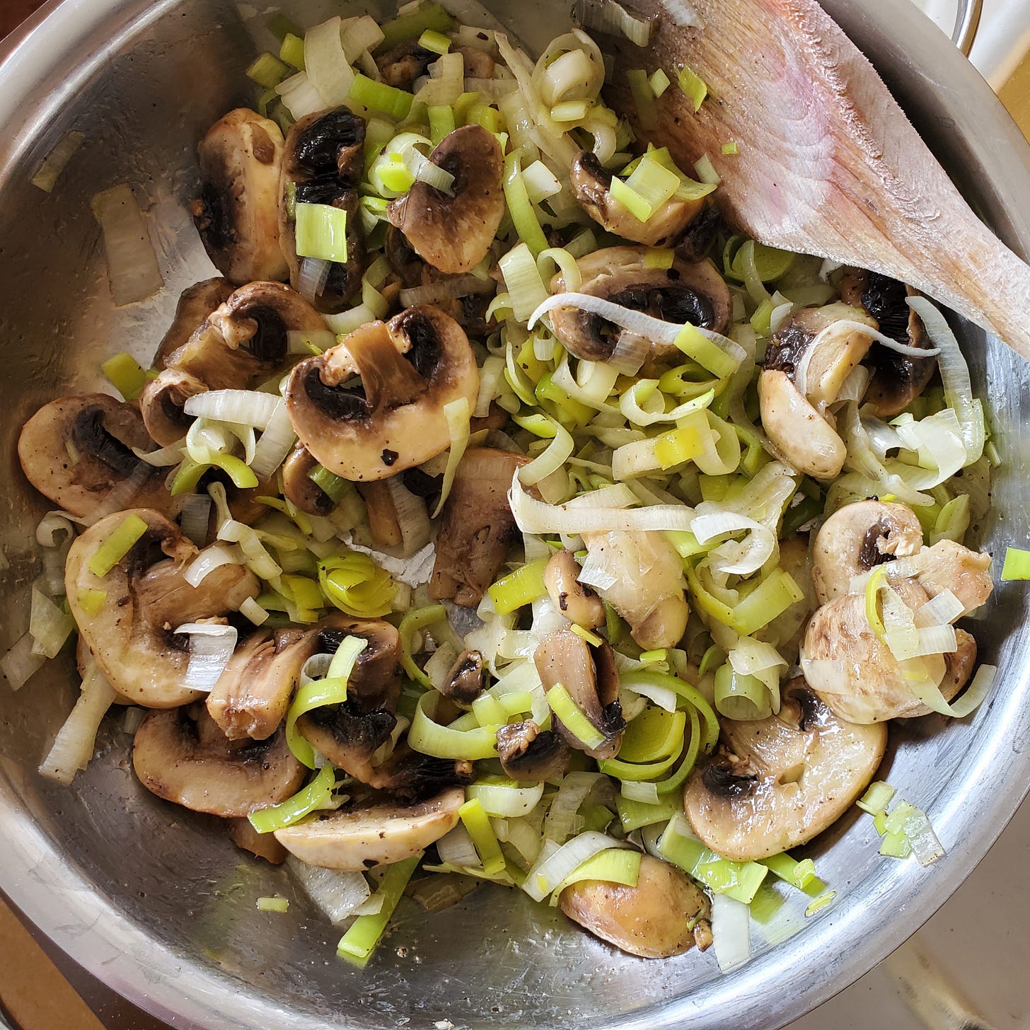 Leeks and mushrooms in a steel frying pan with a wooden spoon. 