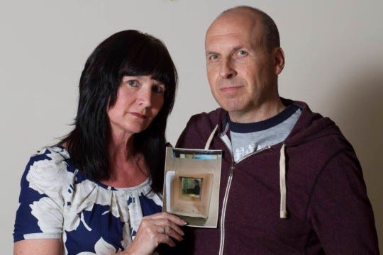 Sheila Sillery-Walsh, 48, left, with partner Paul Rice, 50, right, pictured at home in Birmingham, UK, June 2014. Sheila is holding the ghostly image she took on her iPhone of what appears to be a woman inside an empty cell in the notorious Alcatraz prison off the coast of San Fransisco, California, USA when the couple holidayed there in April 2014.  Ö PIC BY NEWS DOG MEDIA .. +44 (0) 121 246 1932