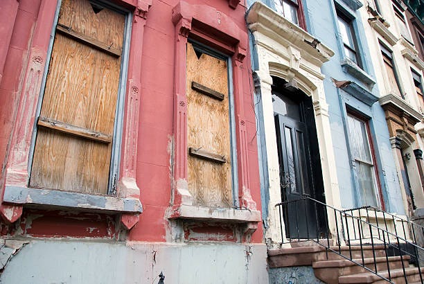 A run down apartment building with the windows boarded up and cracks in the concrete. 