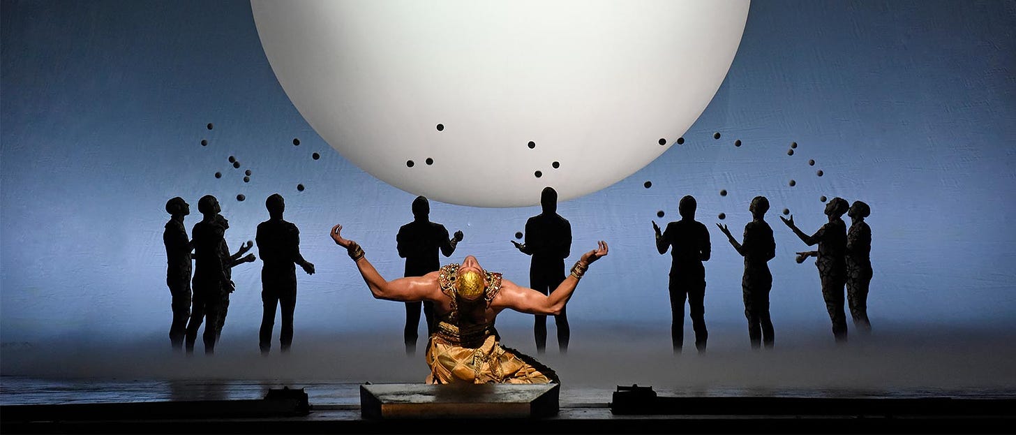 Picture shows a man in Ancient Egyptian dress in the foreground, with silhouetted figures in the background juggling. In the extreme background, a large white disk (presumably representing the Aten, which was represented by a disk) is shown on a field of blue.