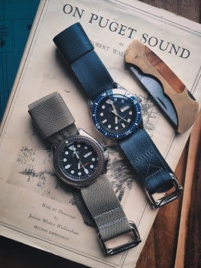 two seiko diver watches, one on an origional green ZA strap and the other on a grey ZA strap on the book On Puget Sound with a pocket knife