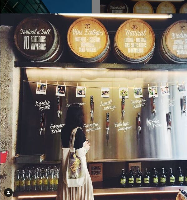 Girl standing in front of natural wine barrels and taps to fill wine to-go