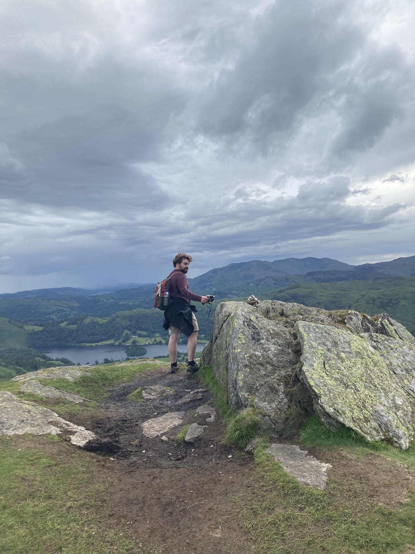 The author stands on top of a hill looking out over a lake and town in the Lake District.