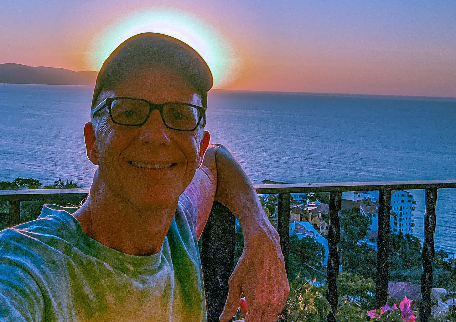 A smiling Michael standing on a patio in Puerto Vallarta, Mexico, with the ocean and sunset behind him.